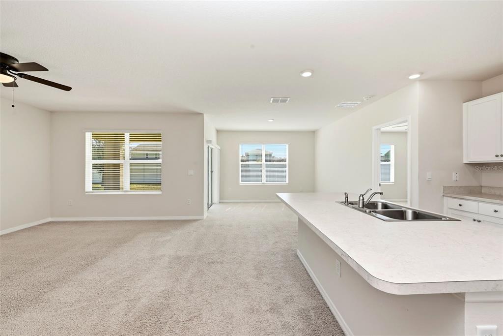 An open-concept living area features beige carpeting, a kitchen island with a sink, and windows — 2725 DUMONT LANE, TAVARES, FL