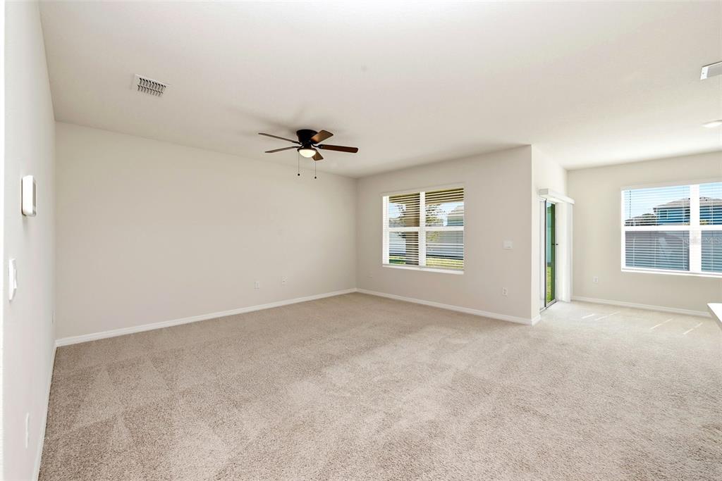 An empty living room features beige carpet, light walls, a ceiling fan, and large windows — 2725 DUMONT LANE, TAVARES, FL