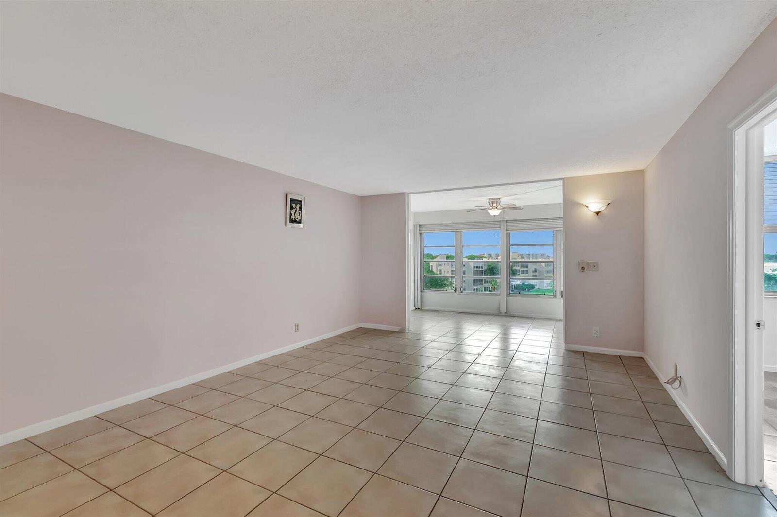 An empty living room with light-colored walls, beige tile flooring, and large windows overlooking buildings — 14623 Bonaire Boulevard # 502, Delray Beach FL 33446, DELRAY BEACH, FL
