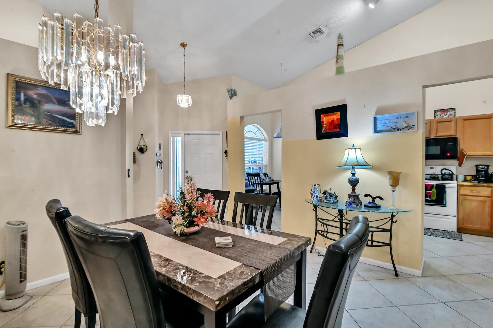A dining room with a crystal chandelier, marble-topped table, and tile flooring leads to a kitchen — 8072 Key West Lane, Boynton Beach FL 33472, BOYNTON BEACH, FL