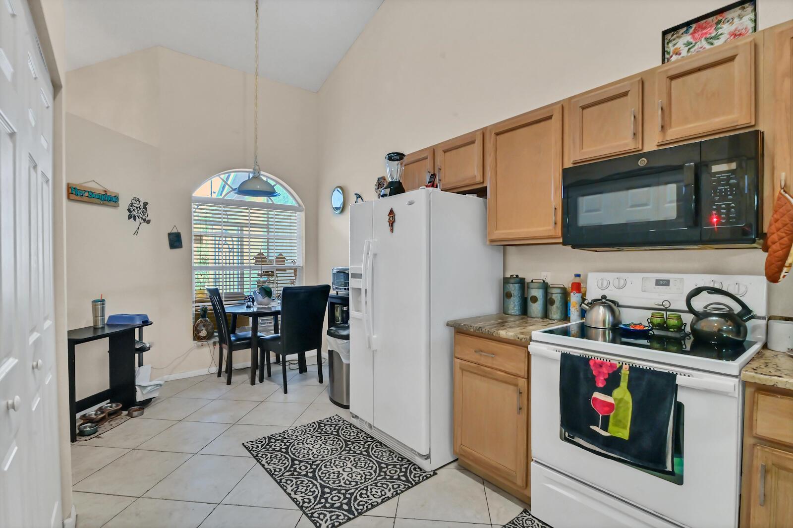 A kitchen features light wood cabinets, white appliances, tile flooring, and a small dining area — 8072 Key West Lane, Boynton Beach FL 33472, BOYNTON BEACH, FL