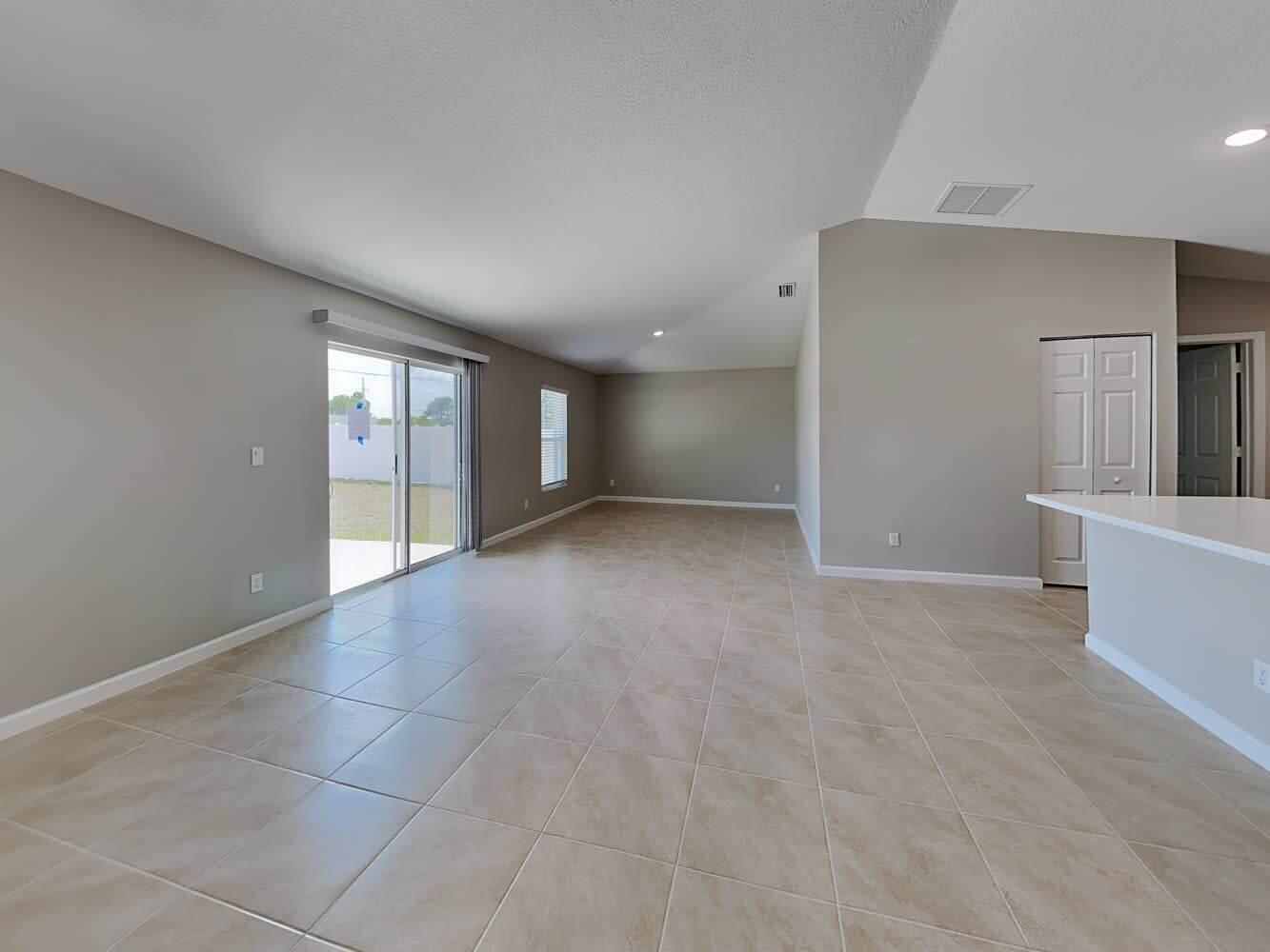 An open-concept living area features light-colored tile flooring, neutral walls, and a sliding glass door — PORT ST. LUCIE, FL