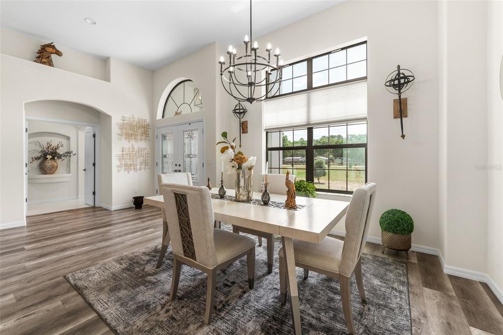 A dining room features a light wood table, upholstered chairs, a chandelier, and large windows — 11645 SW 134TH COURT, DUNNELLON, FL
