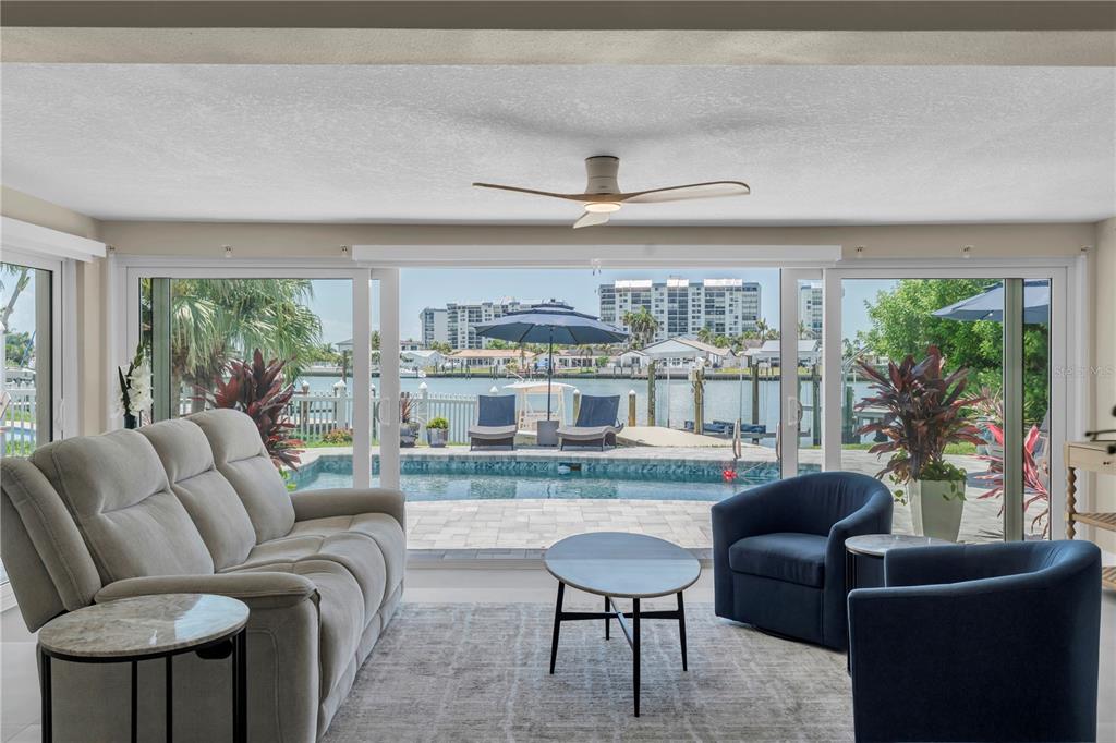 A living room with a sofa and chairs overlooks a swimming pool and a canal — 24 MARINA TERRACE, TREASURE ISLAND, FL
