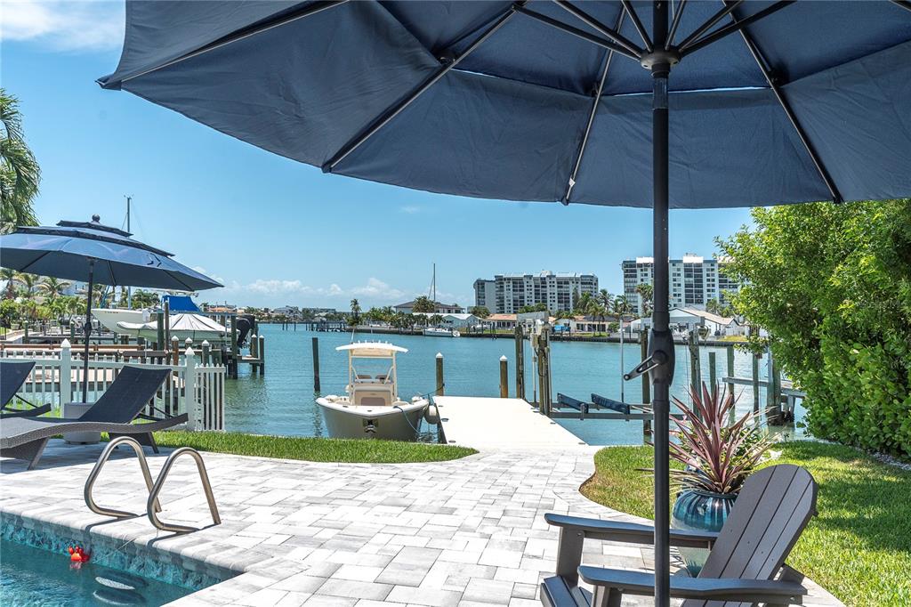 A patio with lounge chairs and umbrellas overlooks a swimming pool and a boat dock — 24 MARINA TERRACE, TREASURE ISLAND, FL