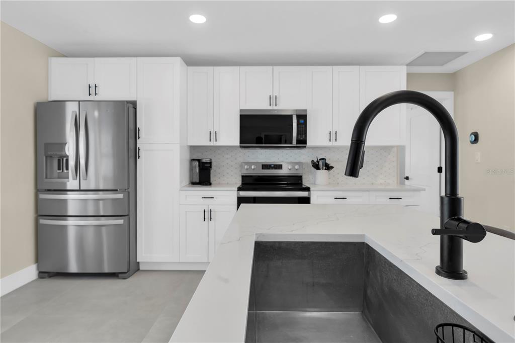 A modern kitchen features white cabinetry, stainless steel appliances, a kitchen island, and a sink — 24 MARINA TERRACE, TREASURE ISLAND, FL