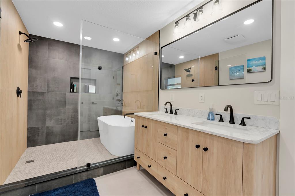 A modern bathroom features a double vanity, a glass-enclosed shower, and a freestanding soaking tub — 24 MARINA TERRACE, TREASURE ISLAND, FL