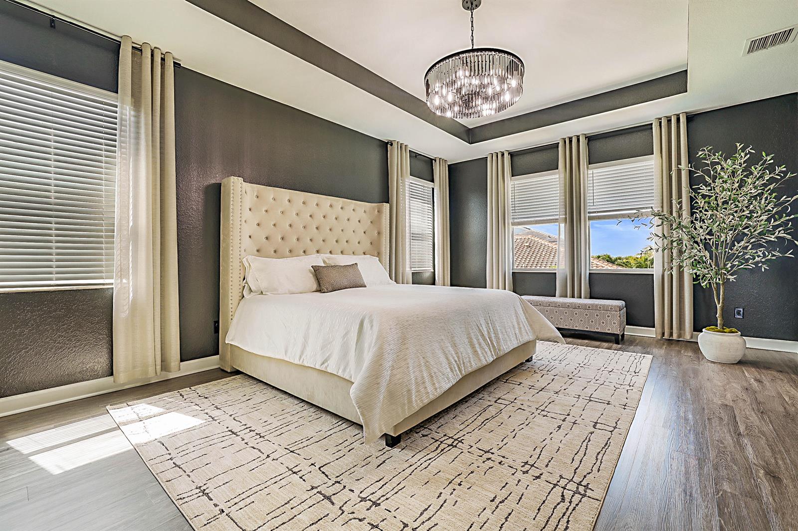 A bedroom features dark walls, a tufted beige headboard, a chandelier, and a patterned rug — 19671 Split Rail Run, Loxahatchee FL 33470, LOXAHATCHEE, FL