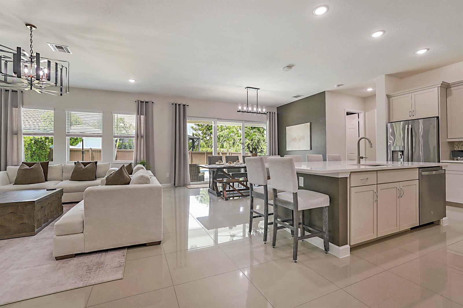 An open-concept living room and kitchen feature light tile floors, neutral furniture, and stainless appliances — 19671 Split Rail Run, Loxahatchee FL 33470, LOXAHATCHEE, FL