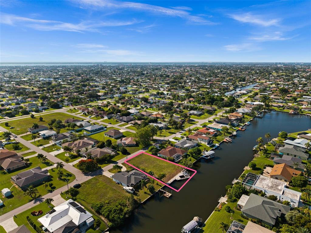 An aerial view shows a vacant waterfront lot outlined in pink along a canal — 3022 SE 6TH AVENUE, CAPE CORAL, FL