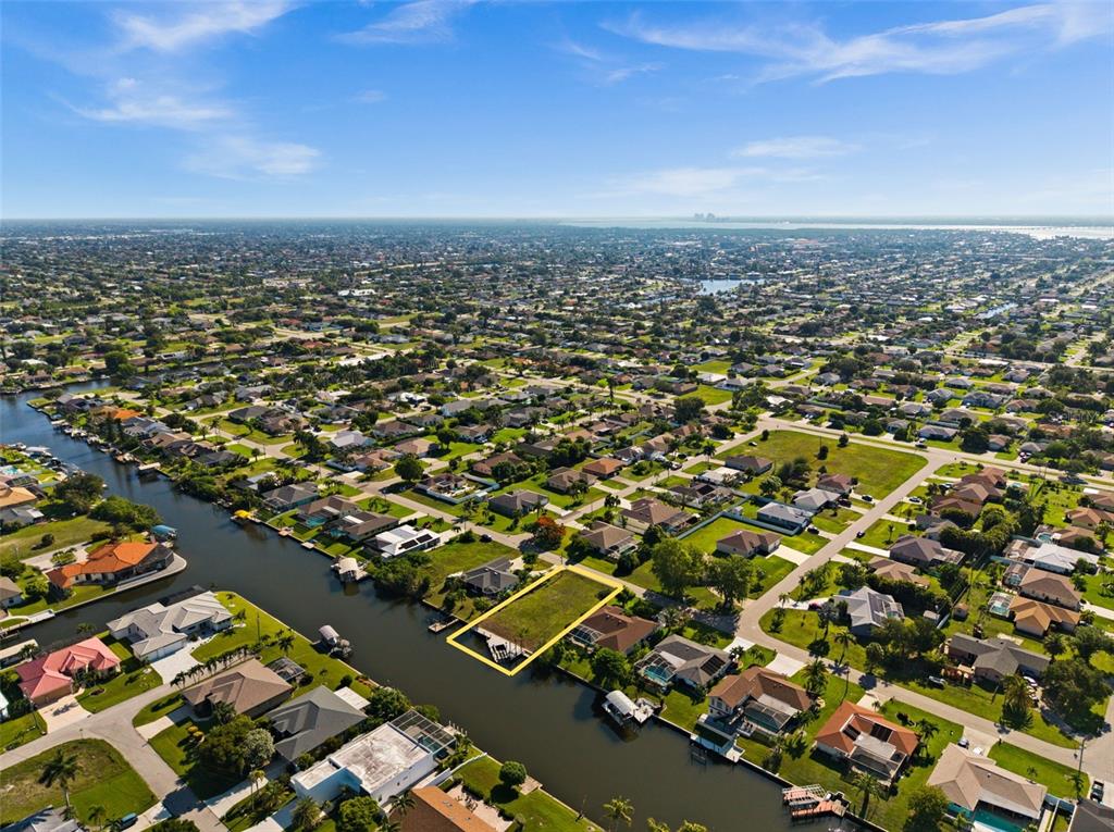An aerial view shows a vacant waterfront lot outlined in yellow within a residential neighborhood — 3022 SE 6TH AVENUE, CAPE CORAL, FL