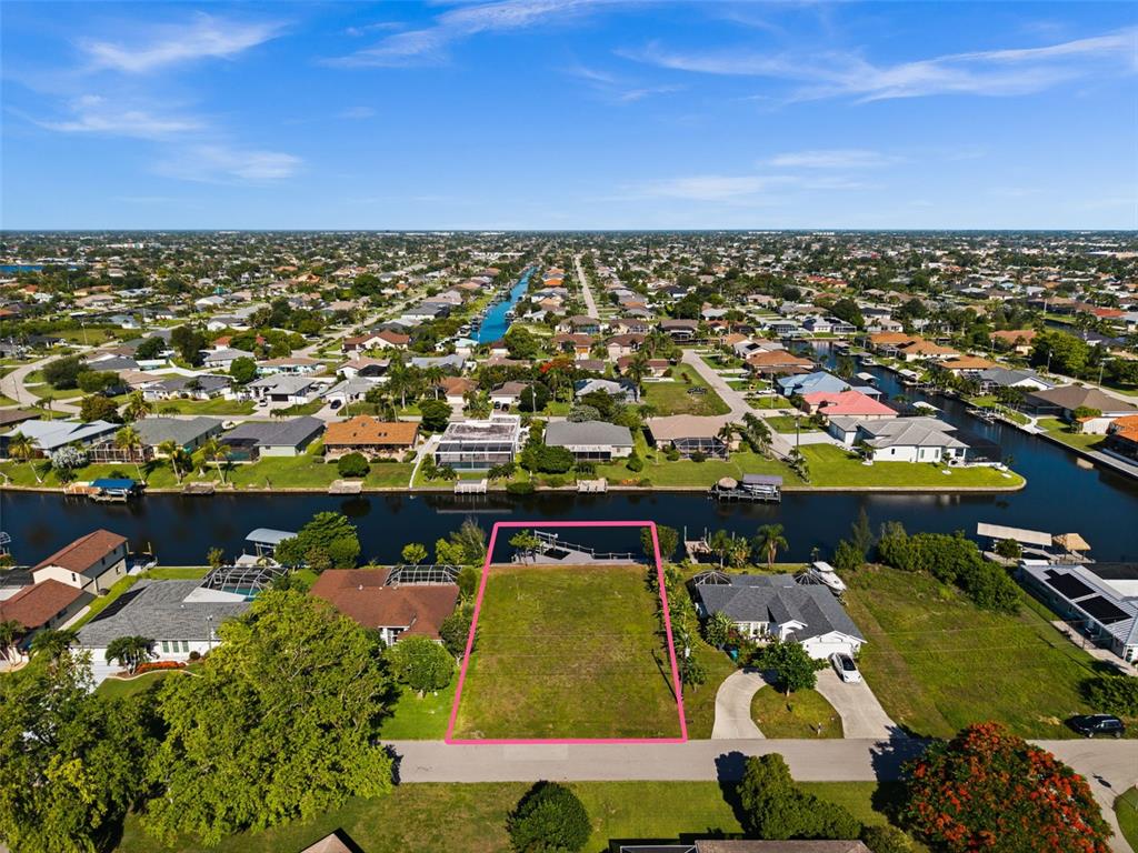 An aerial view shows a vacant waterfront lot outlined in pink along a canal — 3022 SE 6TH AVENUE, CAPE CORAL, FL