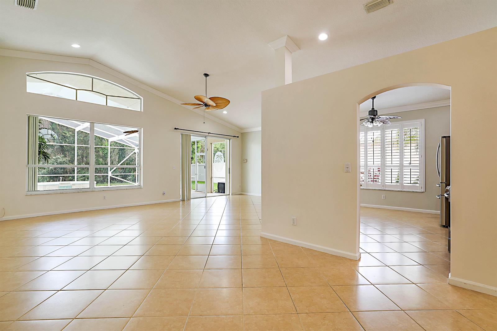 A spacious living area with beige tile floors, vaulted ceilings, and an arched kitchen entryway — 992 SE Westminster Place, Stuart FL 34997, STUART, FL