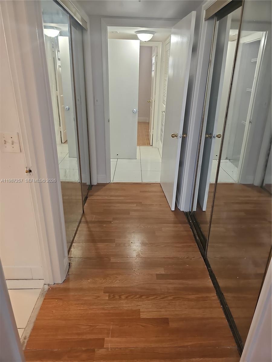 A hallway with hardwood flooring features mirrored closet doors and leads to a tiled room — 3301 Spanish Moss Ter # 708, Lauderhill FL 33319, LAUDERHILL, FL