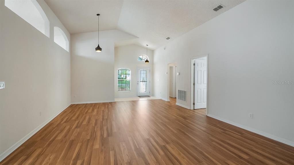 An empty room with vaulted ceilings, wood-look flooring, and a front entryway — 4127 CAPLAND AVENUE, CLERMONT, FL