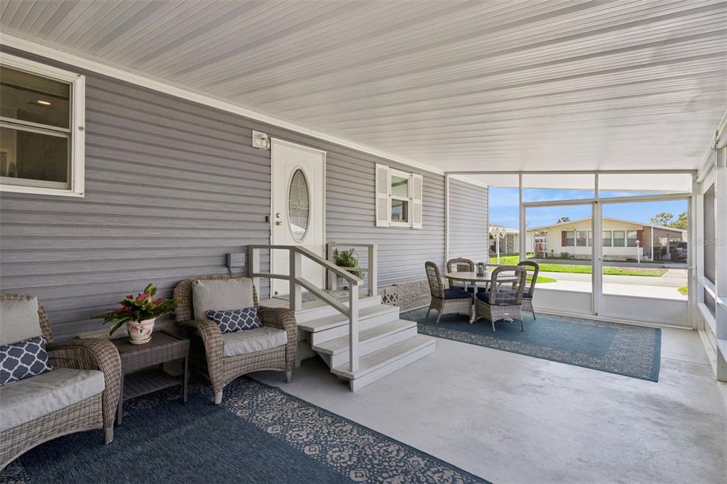 A covered, screened-in porch features gray siding, concrete flooring, and outdoor furniture — 8568 BREEZE HILL DRIVE, LAKE WALES, FL