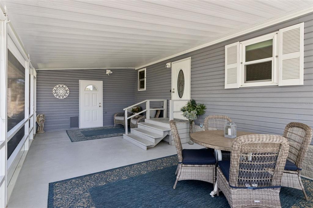 A covered porch features gray siding, a dining set, and two exterior doors — 8568 BREEZE HILL DRIVE, LAKE WALES, FL