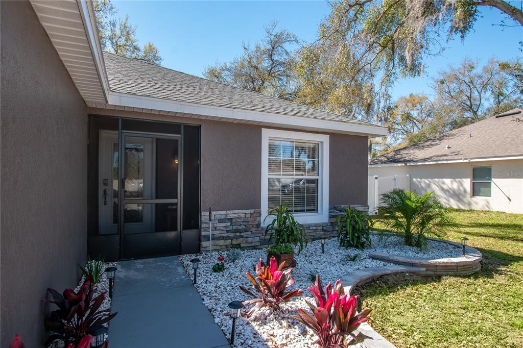 A house exterior features a stone-accented facade, a screened entryway, and a white rock garden — 2309 ANGEL FISH LOOP, LEESBURG, FL