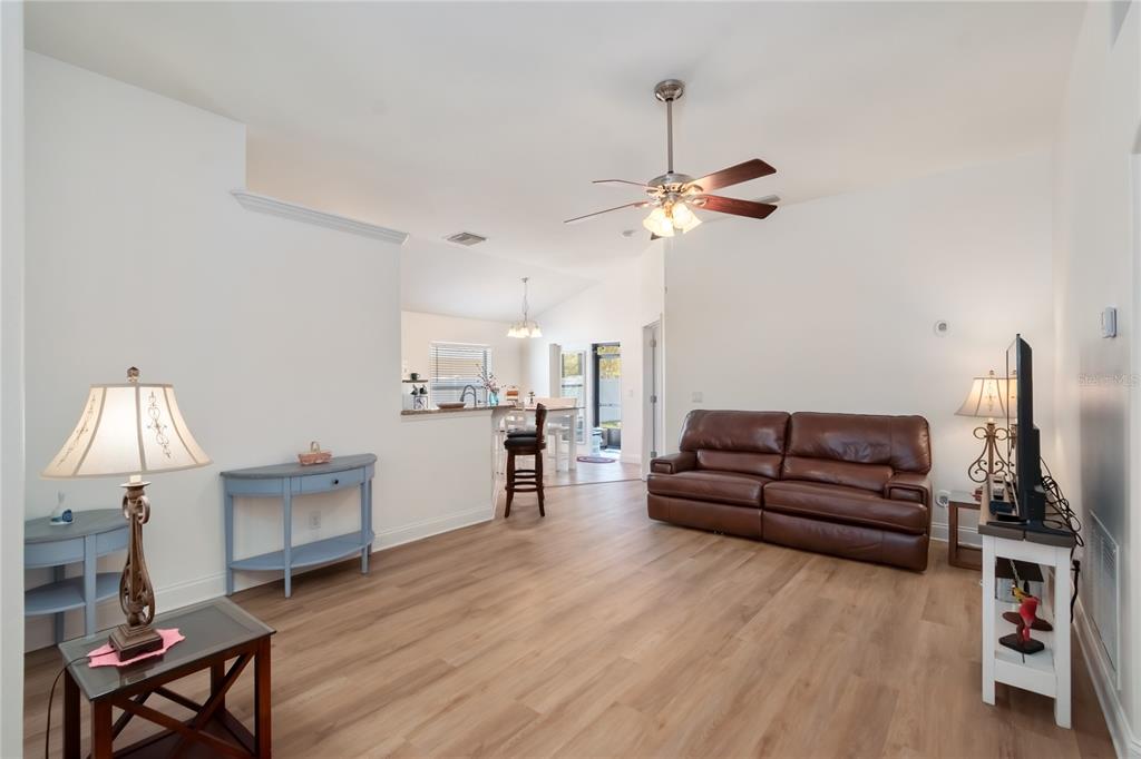 A living room with wood-look flooring, a brown leather sofa, and an open kitchen view — 2309 ANGEL FISH LOOP, LEESBURG, FL