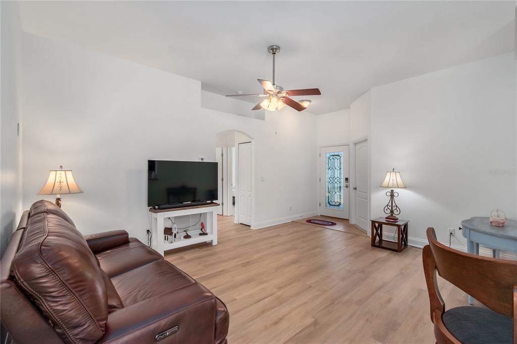 A living room with light wood flooring, a brown leather sofa, and a ceiling fan — 2309 ANGEL FISH LOOP, LEESBURG, FL