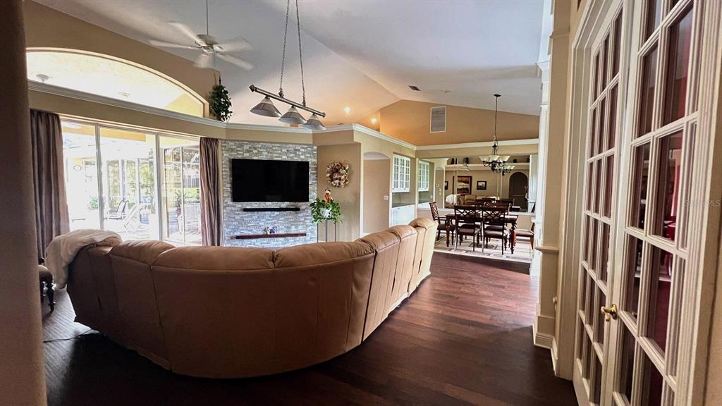 A living room with a stone fireplace, curved sectional sofa, and an adjacent dining area — 8333 EAGLE LAKE DRIVE, SARASOTA, FL