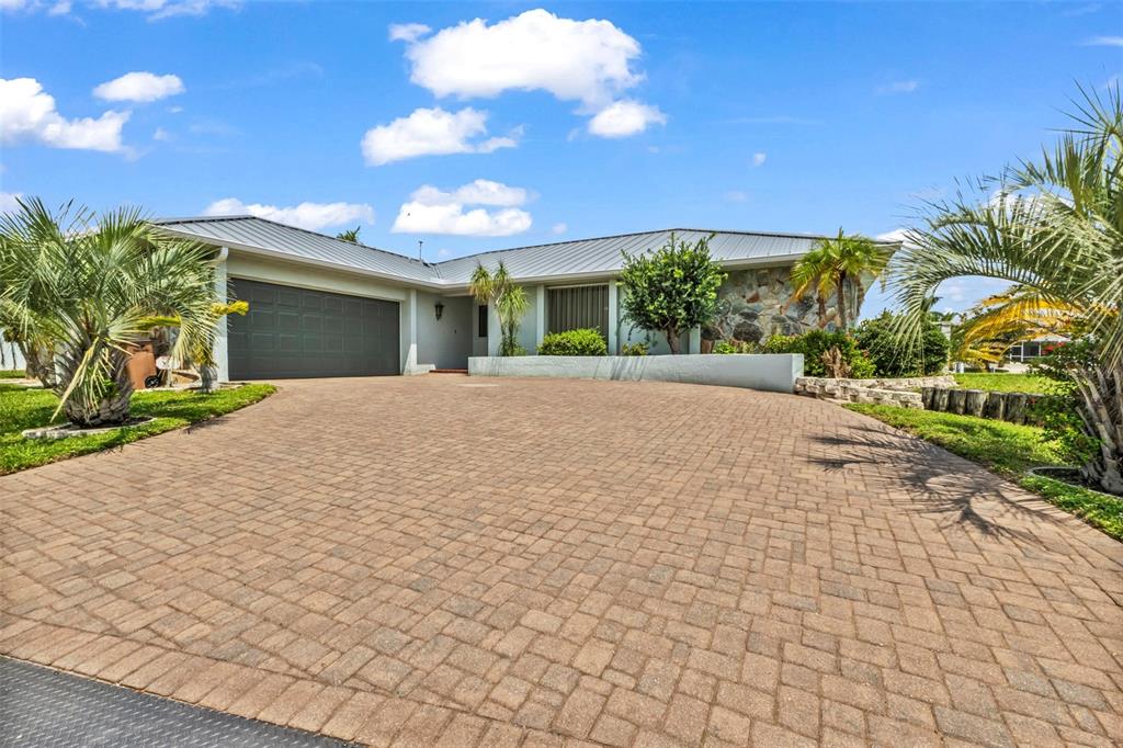 A single-story house with a paved driveway, metal roof, and stone facade exterior — 704 BIMINI LANE, PUNTA GORDA, FL