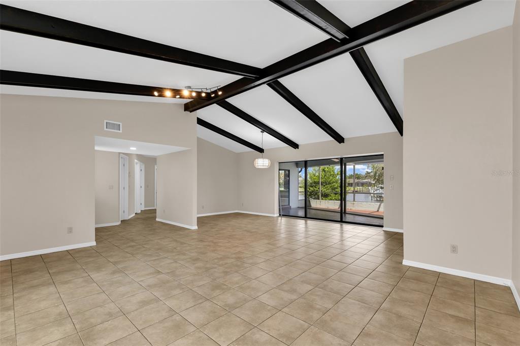 An empty living room features vaulted ceilings with dark exposed beams and tile flooring — 704 BIMINI LANE, PUNTA GORDA, FL