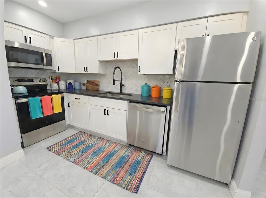 A kitchen features white cabinets, stainless steel appliances, a dark countertop, and a colorful rug — 2941 SHORE DRIVE UNIT A, SAFETY HARBOR, FL