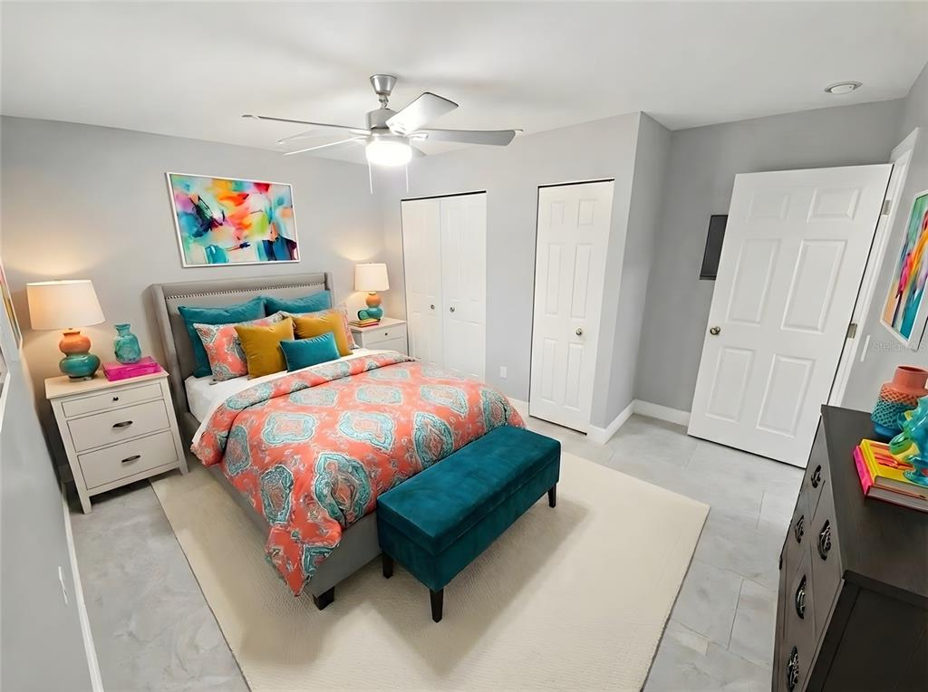 A bedroom features a bed with colorful bedding, a teal bench, and light gray walls — 2941 SHORE DRIVE UNIT A, SAFETY HARBOR, FL