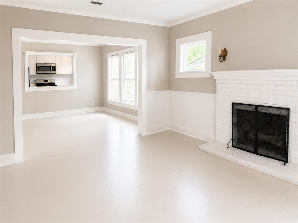 A living room with a white brick fireplace, light-colored wood floors, and a pass-through window — 712 MCKENZIE STREET, LEESBURG, FL