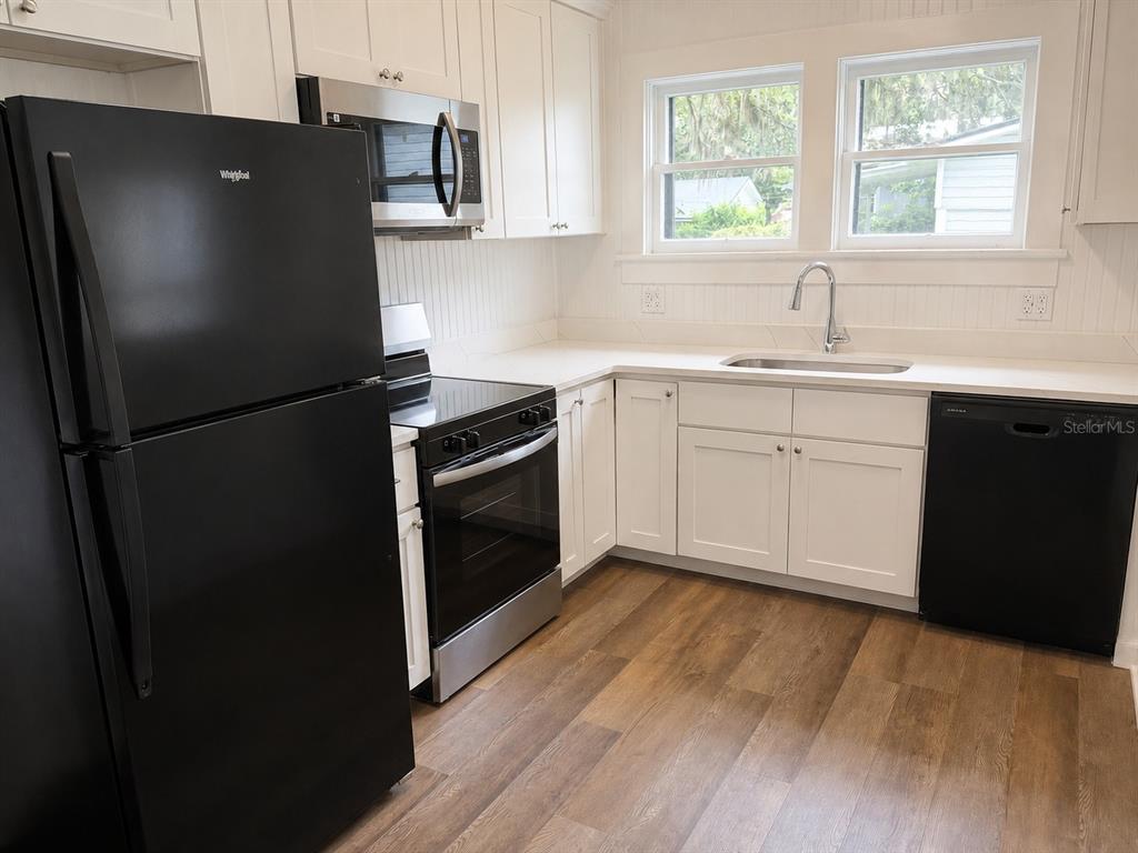 A kitchen features white cabinets, black appliances, a stainless steel sink, and wood-look flooring — 712 MCKENZIE STREET, LEESBURG, FL