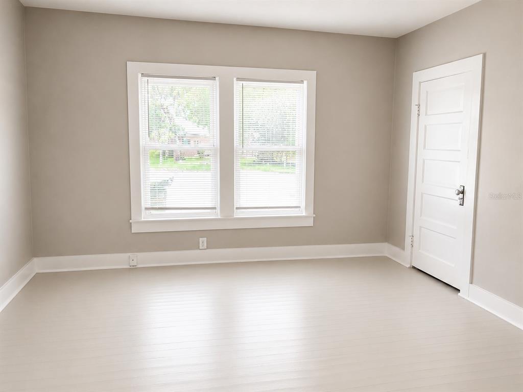 An empty room with light-colored walls, white trim, a window with blinds, and a door — 712 MCKENZIE STREET, LEESBURG, FL
