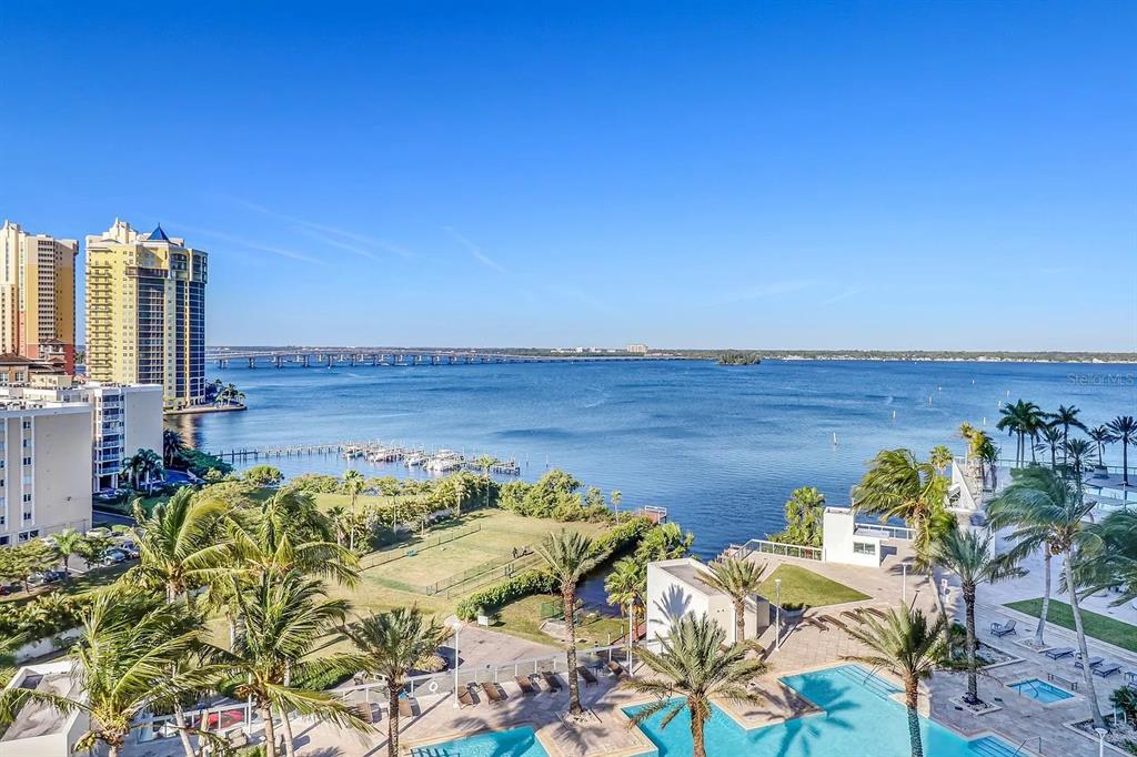 An elevated view of a waterfront property featuring a swimming pool, palm trees, and bridge — 3000 OASIS GRAND BOULEVARD UNIT 1002, FORT MYERS, FL