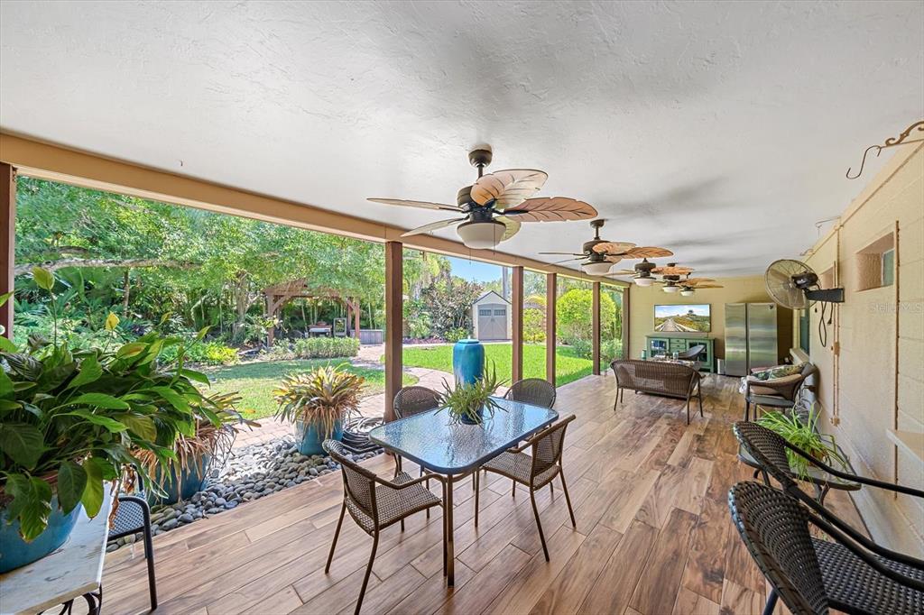 A covered patio features wood-look tile flooring, multiple ceiling fans, and a view of a yard — 2462 CLEMATIS STREET, SARASOTA, FL