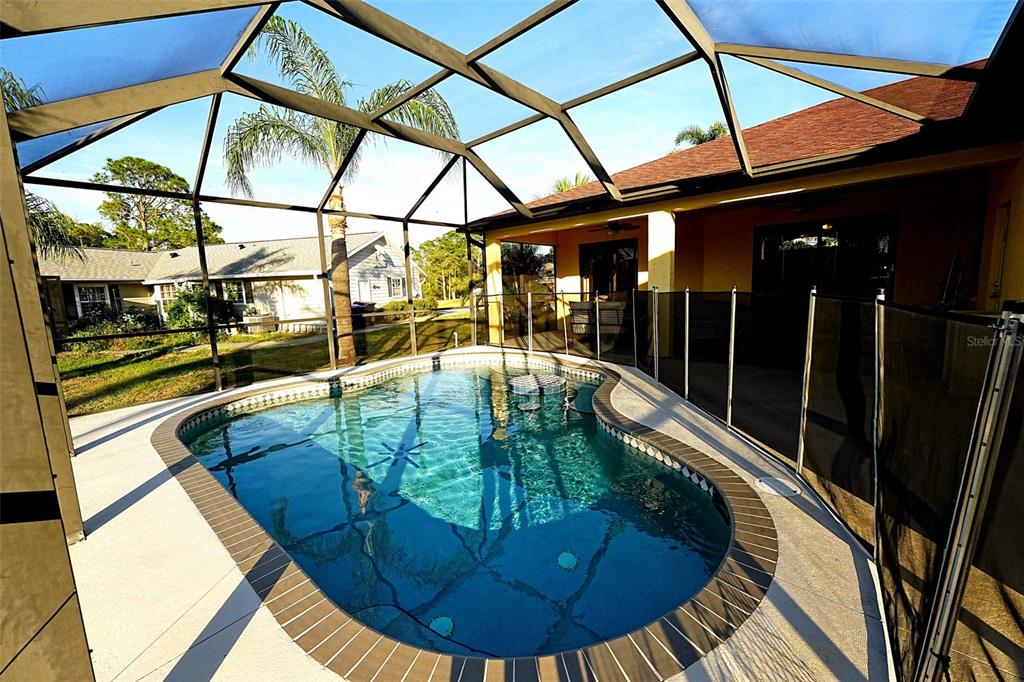 A screened-in swimming pool with a safety fence sits on a patio beside a house — 3522 RENAULT CIRCLE, NORTH PORT, FL