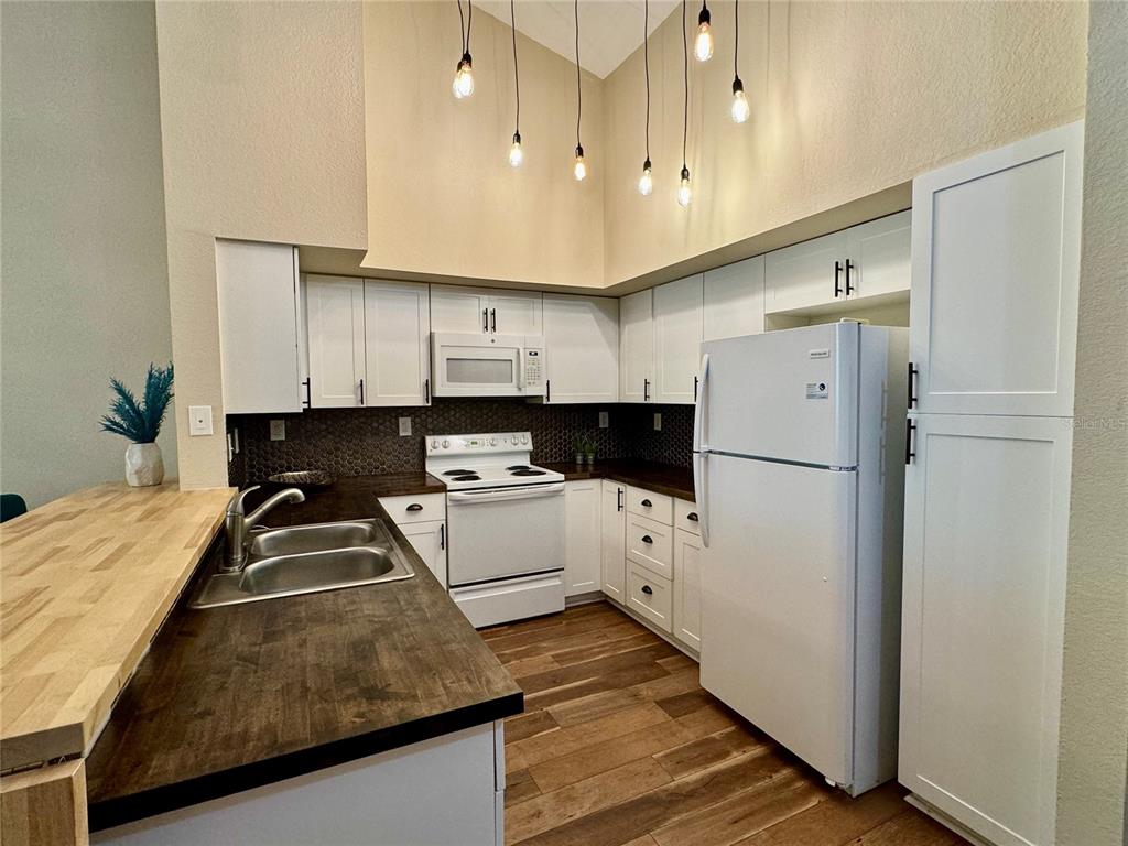 An open-concept living area features wood-look flooring, a kitchen breakfast bar, and modern light fixtures — 4106 CENTRAL SARASOTA PARKWAY UNIT # 1028, SARASOTA, FL