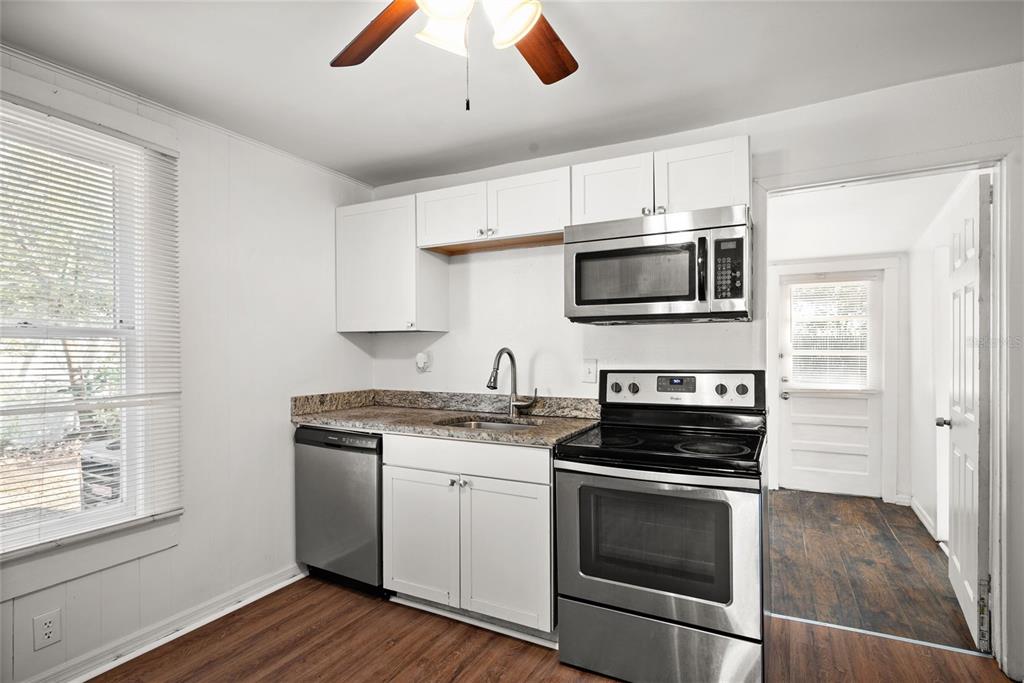 A kitchen features white cabinets, stainless steel appliances, granite countertops, and wood-look flooring — 211 E CLUSTER AVENUE, TAMPA, FL