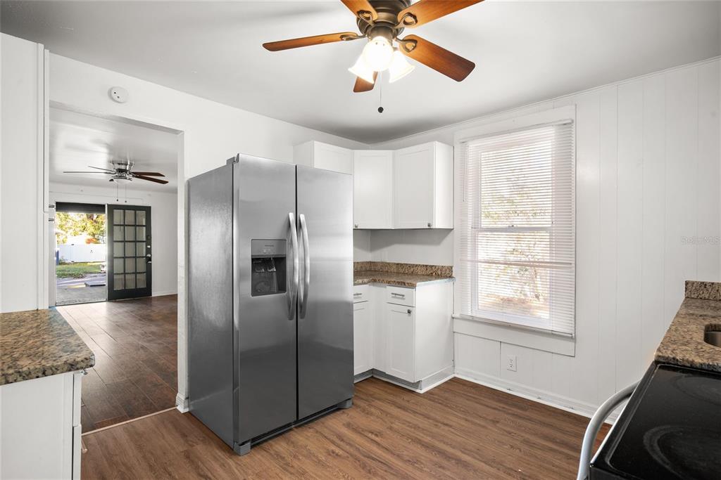 A kitchen features white cabinets, granite countertops, a stainless steel refrigerator, and wood-look flooring — 211 E CLUSTER AVENUE, TAMPA, FL