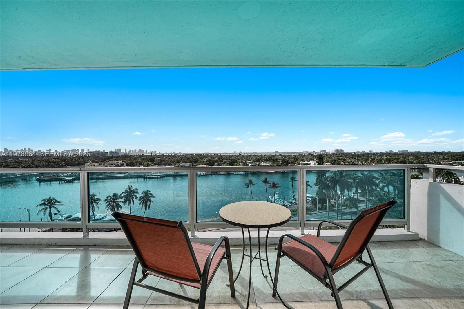 A balcony features two chairs, a small table, and a view of the water — 5101 Collins Ave # 11B, Miami Beach FL 33140, MIAMI BEACH, FL
