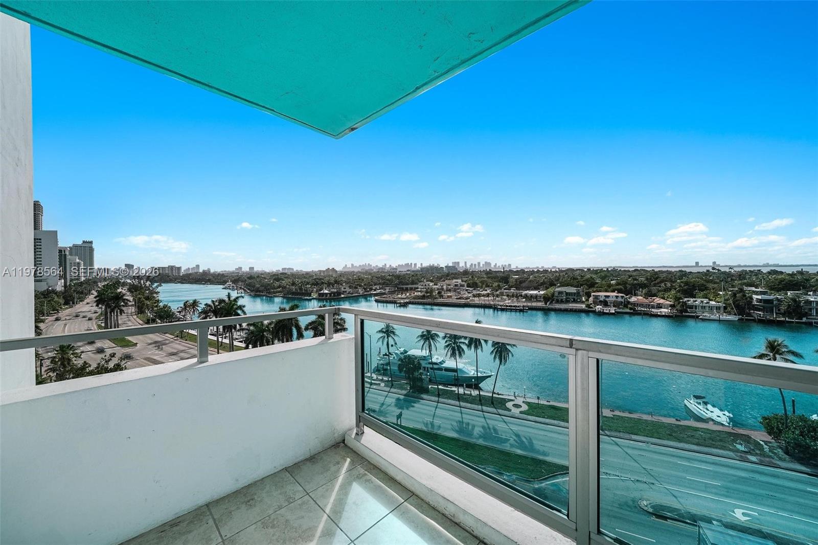 A balcony overlooks a waterway, a road, palm trees, and a distant city skyline — 5101 Collins Ave # 11B, Miami Beach FL 33140, MIAMI BEACH, FL