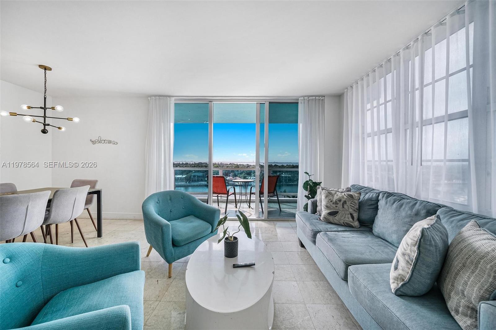 A living and dining area features blue furniture, marble floors, and a balcony with water views — 5101 Collins Ave # 11B, Miami Beach FL 33140, MIAMI BEACH, FL