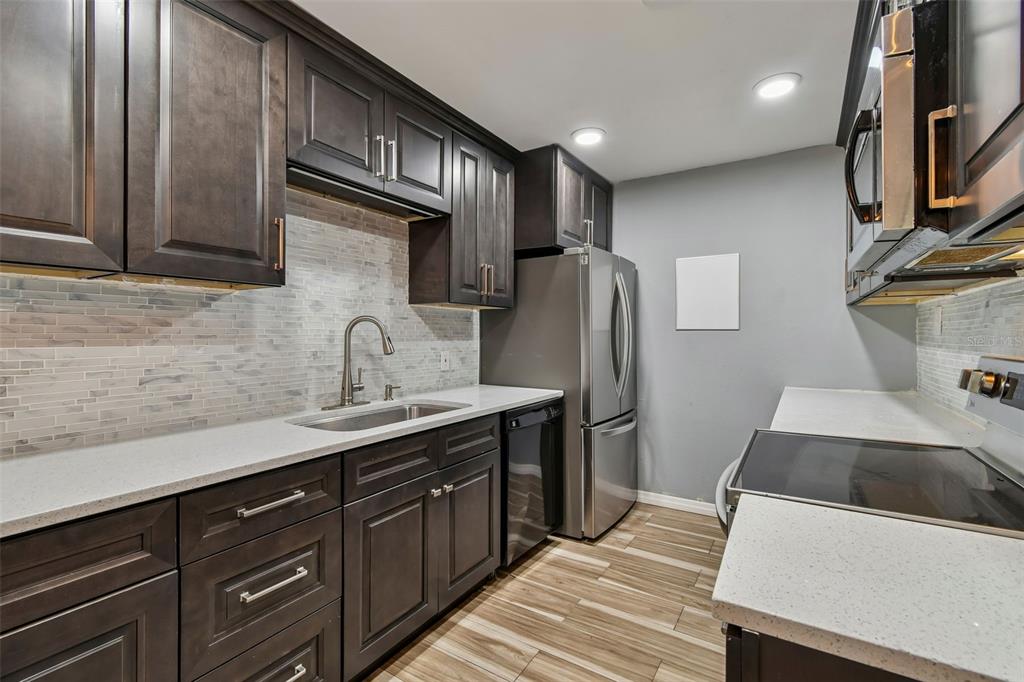 A kitchen features dark wood cabinets, white countertops, stainless steel appliances, and a tiled backsplash — 1695 LEE ROAD UNIT E215, WINTER PARK, FL
