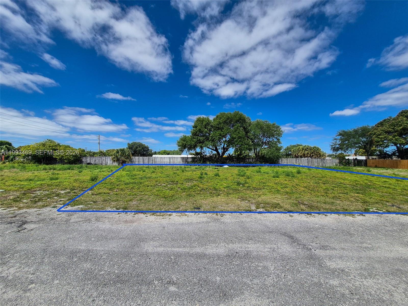 A vacant, grassy rectangular lot is outlined in blue against a clear, sunny sky — NW 19th Ave, Pompano Beach FL 33069, POMPANO BEACH, FL