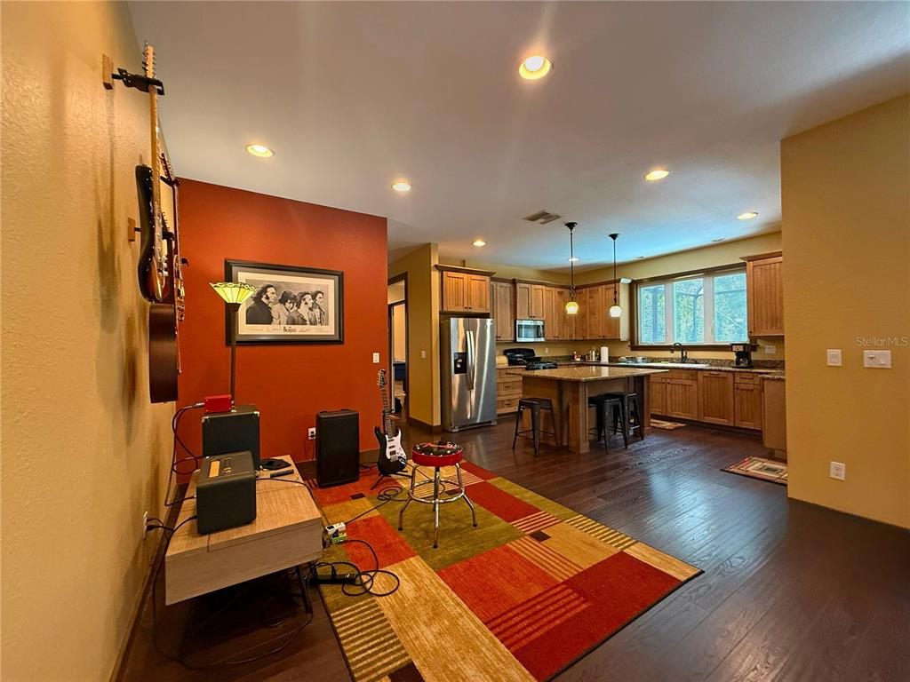A living area with musical instruments and a rug opens into a kitchen with wood cabinets — 11691 SW 52ND AVENUE, OCALA, FL