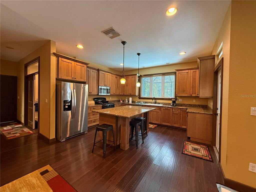 A kitchen features wood cabinets, granite countertops, a center island with stools, and hardwood floors — 11691 SW 52ND AVENUE, OCALA, FL