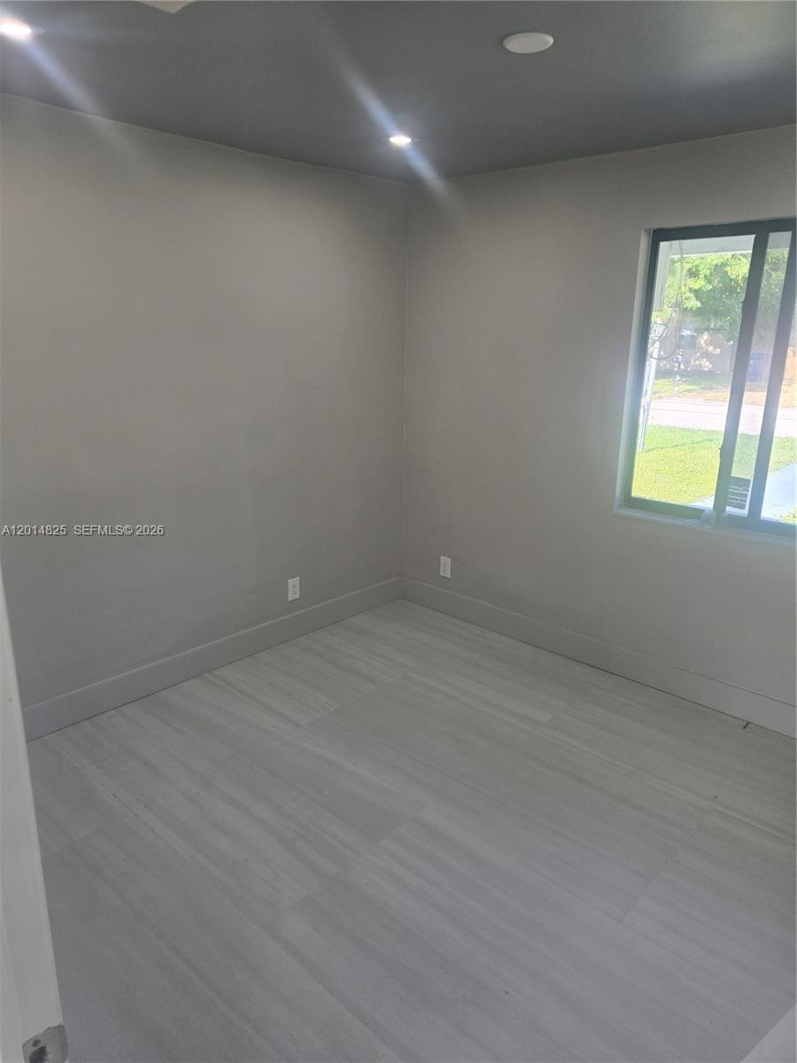 A small bedroom features light gray walls, wood-look flooring, and a single window — 3300 SE 6th St, Pompano Beach FL 33062, POMPANO BEACH, FL