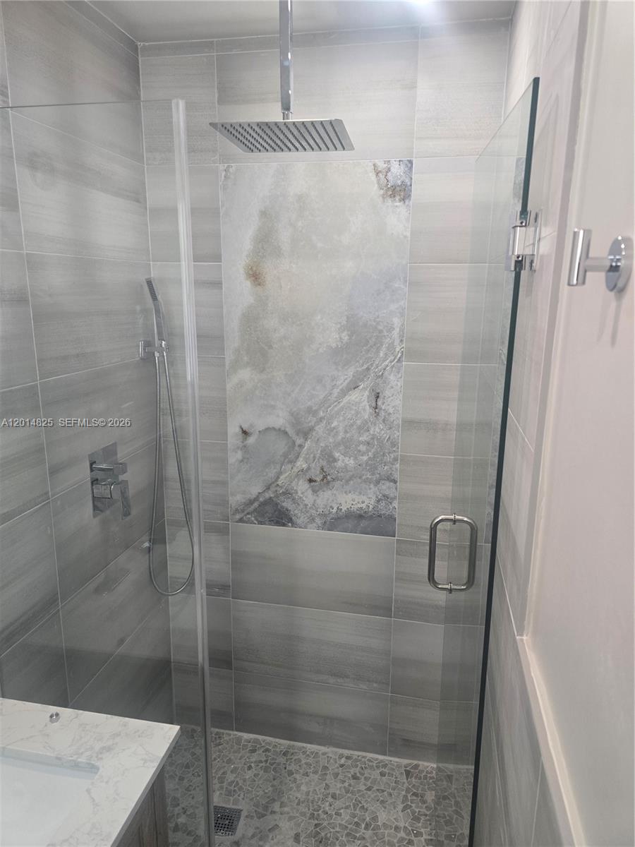 A walk-in shower features gray horizontal wall tiles, a marble-look accent panel, and pebble flooring — 3300 SE 6th St, Pompano Beach FL 33062, POMPANO BEACH, FL
