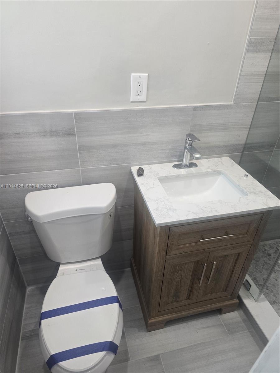 A bathroom features a white toilet, a wood vanity with a marble countertop, and gray tiles — 3300 SE 6th St, Pompano Beach FL 33062, POMPANO BEACH, FL