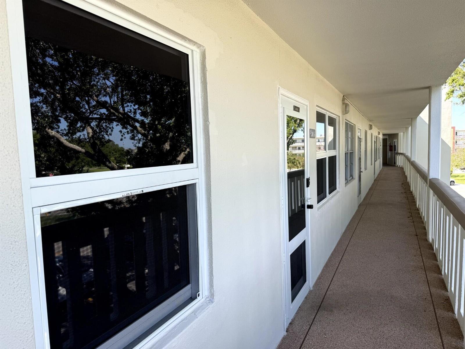 An exterior walkway of a multi-story building with white doors, windows, and a metal railing — 3016 Ashby C # 3016, Deerfield Beach FL 33442, DEERFIELD BEACH, FL