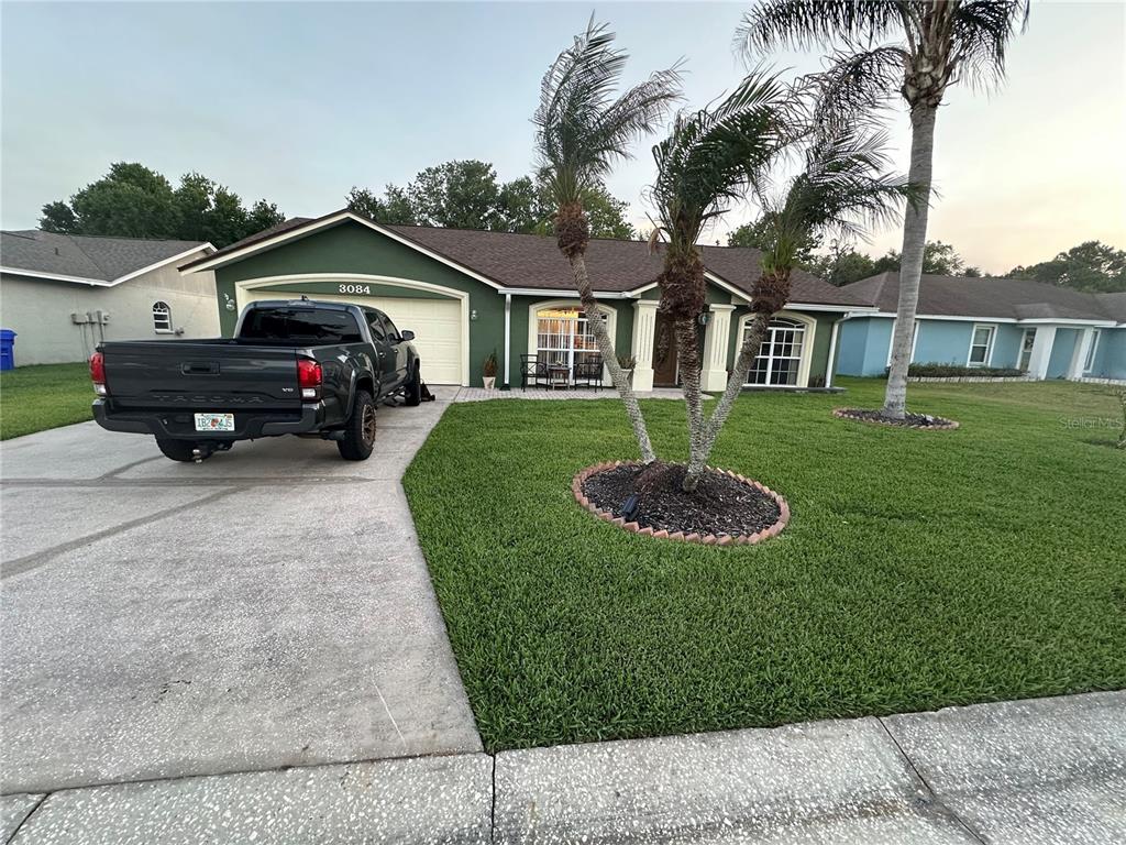 A green single-story house with a driveway, a dark pickup truck, and palm trees — 3084 THOROUGHBRED LOOP W, LAKELAND, FL